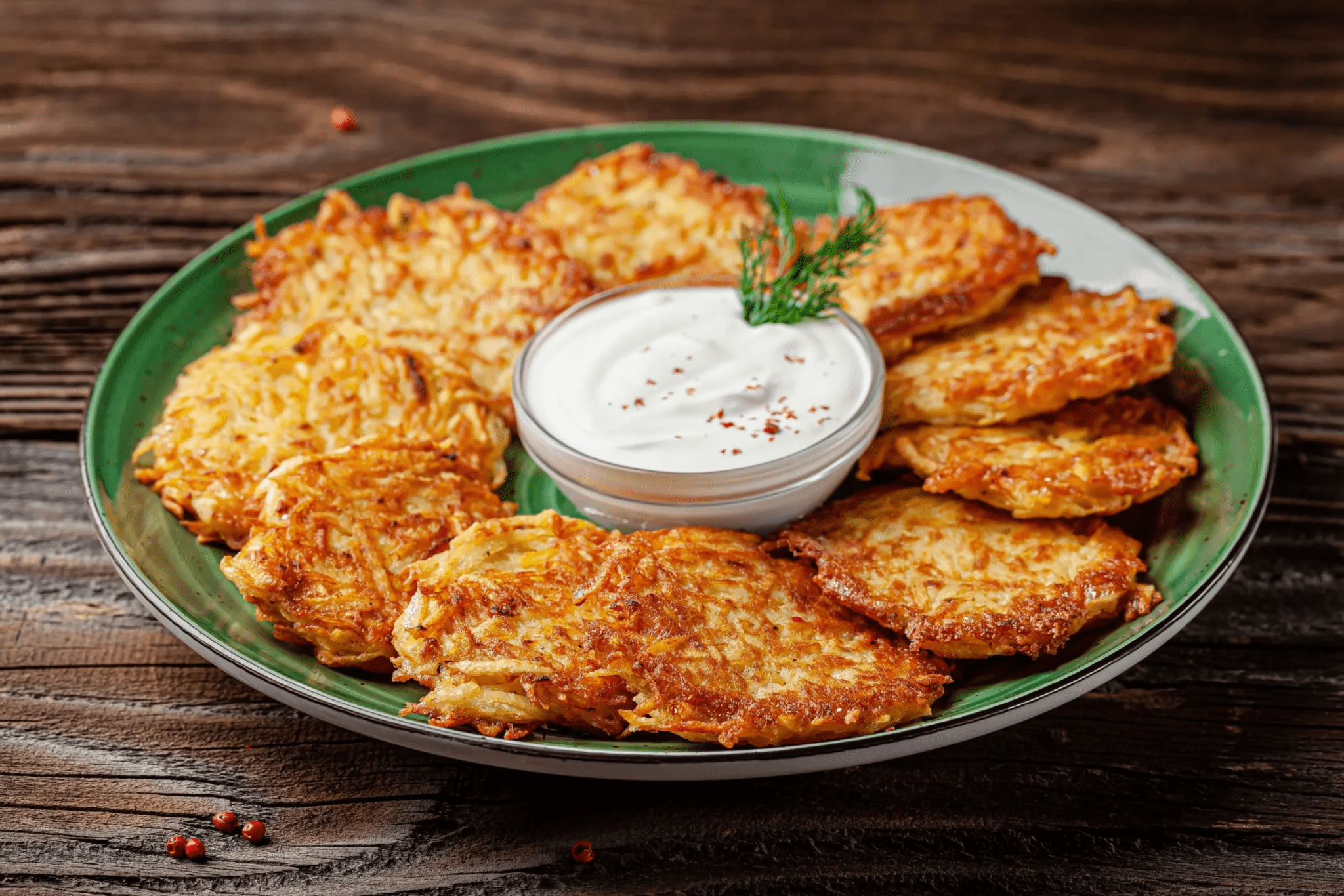 Стопка золотистых дерунов со сметаной и зеленью на тарелке