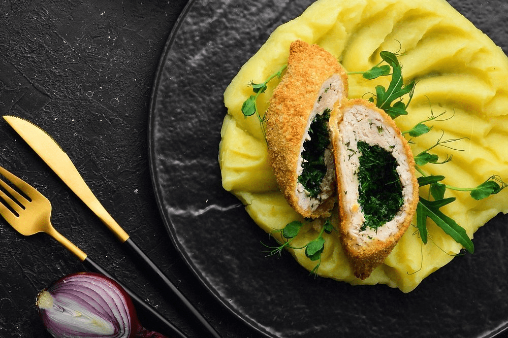 Разрезанная котлета по-киевски, из которой вытекает масло, поданная с картофельным пюре