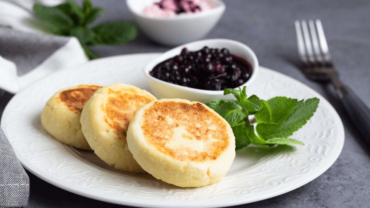 Стопка румяных сырников, политых медом и украшенных ягодами